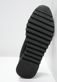 Černá podrážka tenisek s výraznými horizontálními drážkami, texturovaný gumový materiál a robustní design, poskytující trakci a odolnost.