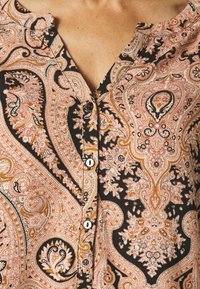 Knap-shirt med paisley-mønster i nuancer af pink, creme og brun på en sort baggrund; glat stof med en rund krave.