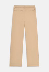 Beige raka byxor med bakfickor i vävt material och en liten rektangulär logotyp på höger ficka mot vit bakgrund.