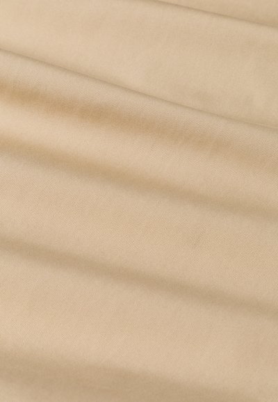 Beżowy materiał o gładkiej fakturze, z subtelnym połyskiem, z drapowanymi fałdami tworzącymi miękkie linie na powierzchni. Brak wzorów lub akcentów.