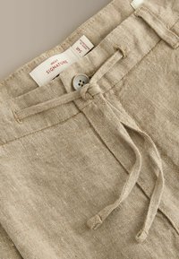 Pantalon en lin beige avec fermeture par bouton et cordon en tissu, avec une étiquette indiquant "Next Signature" et taille 34R.