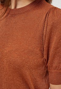 Rostfärgad tröja i pulloverstil med texturerad knit, ribbad halsringning och korta puffärmar med elastiska manschetter. Glittrande tråddetalj.