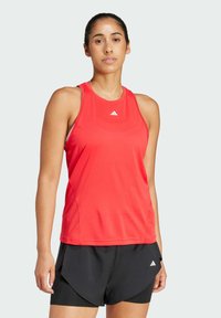 Top atletico rosso senza maniche con scollatura rotonda e design a schiena scoperta, realizzato in materiale leggero, abbinato a pantaloni corti neri con una fessura laterale.