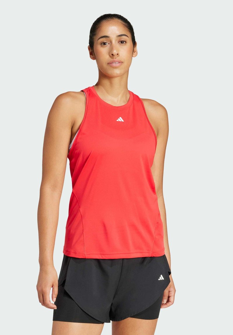 Top atletico rosso senza maniche con scollatura rotonda e design a schiena scoperta, realizzato in materiale leggero, abbinato a pantaloni corti neri con una fessura laterale.