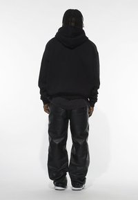 Svart oversized hoodie med dragsko i huvan, tillsammans med löst sittande svarta läderbyxor. Tyget ser glatt ut; silhuetten är avslappnad.