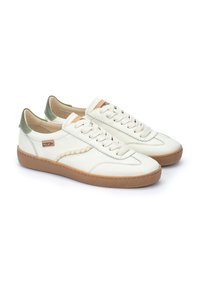 Baskets en cuir blanc avec une semelle crème, des accents verts au niveau du talon et un détail orange contrastant sur la languette. Présente des coutures en textile.