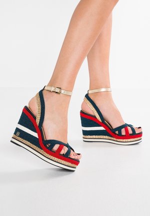 Sandały na koturnie z granatowej, czerwonej i białej plecionej tkaniny, złotym paskiem w kostce oraz plecionym jutowym detalem na wielokolorowej platformie.