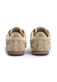 Beżowe, zamszowe buty casual widziane od tyłu, pokazujące szczegóły przeszyć i małe ciemne logo na każdej pętli na pięcie.