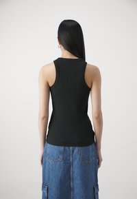 Black ribbed tank top with a fitted design and round neckline, paired with a denim midi skirt featuring patch pockets and a soft texture.