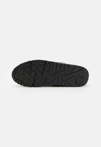 Semelle extérieure en caoutchouc noir d'une chaussure Nike avec des crampons carrés et un motif en zigzag le long du bord de la semelle.