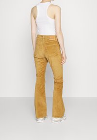 Beige Cord-Pants mit weitem Bein, hoher Taille und dezenter Textur. Mit einem Patch am hinteren Bund und klassischen Gesäßtaschen.