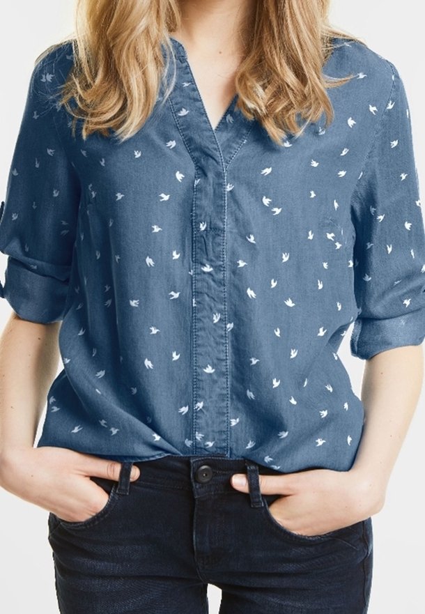 Denimskjorta i blått med vita fågeltryck, korta upprullade ärmar och krage. Mjuk textur och avslappnad passform.