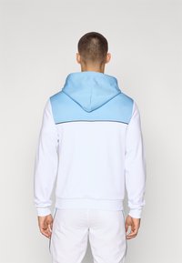 Sudadera con capucha en blanco y azul claro. Presenta un panel contrastante azul en los hombros, mangas largas y un acabado texturizado.