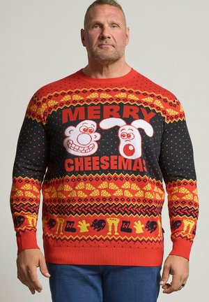 Hombre que lleva un jersey navideño rojo y negro con caras de dibujos animados y texto "Merry Cheesemas" y diseños festivos con patrones.