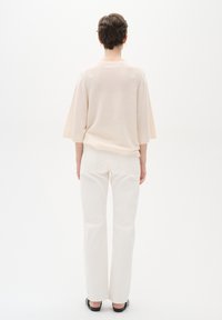 Suéter corto de manga corta en color beige claro con un ajuste holgado, combinado con pantalones blancos de pierna recta. Textura suave con detalles de costura sutiles.