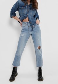 Light blue denim jeans with frayed hems and knee rips; paired with a dark denim button-up shirt and black lace-up boots.