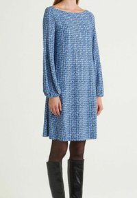 Robe bleue à motifs avec manches longues, encolure ronde et coupe décontractée. Associée à des bottes noires texturées montantes jusqu'aux genoux.