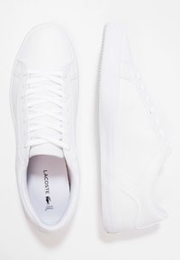 Baskets blanches Lacoste avec lacets, une chaussure vue de dessus, l'autre de côté, affichant un design épuré et minimal.