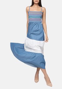 Vestido maxi de mezclilla con corsé fruncido, parte superior azul y sección inferior de ojal bordado blanco. Presenta tirantes delgados y falda acampanada.