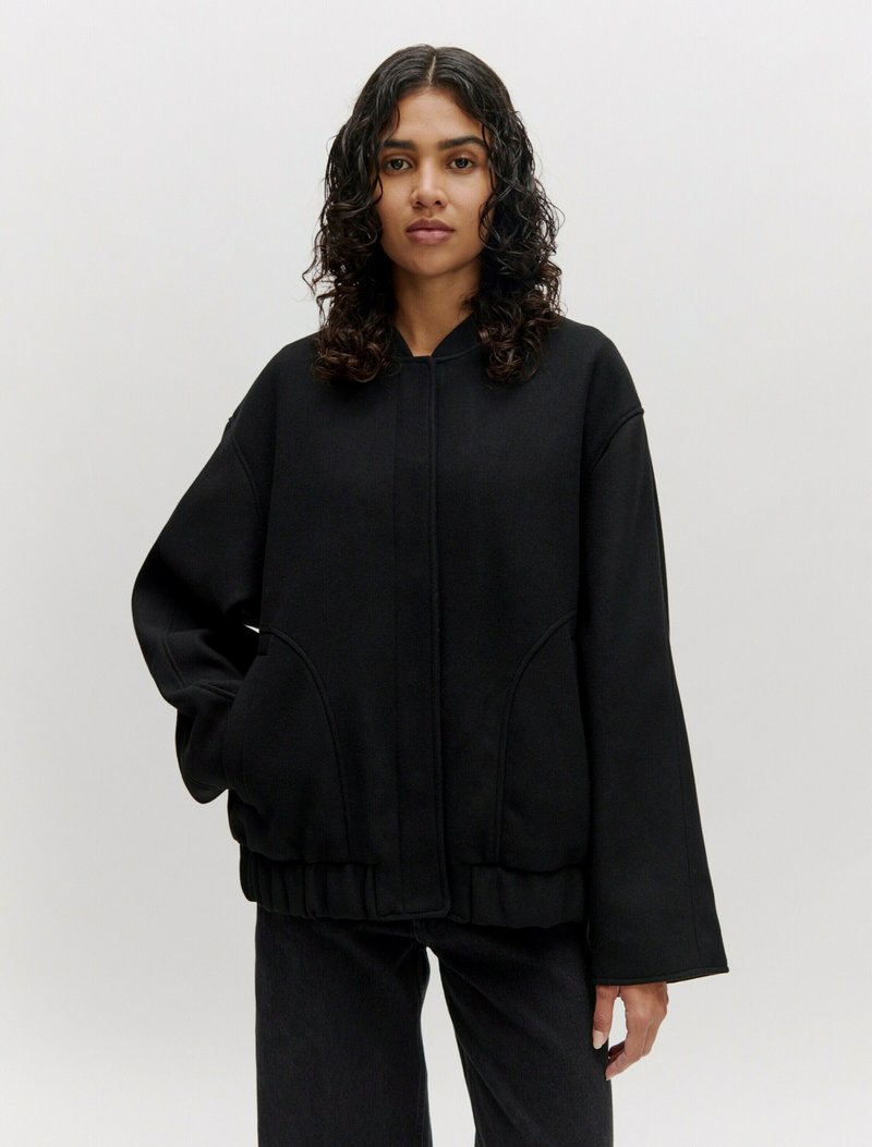 Zwarte oversized hoodie van gestructureerde stof, met een voorste rits, grote zakken en brede mouwen. Versterkt met een geribbelde zoom.