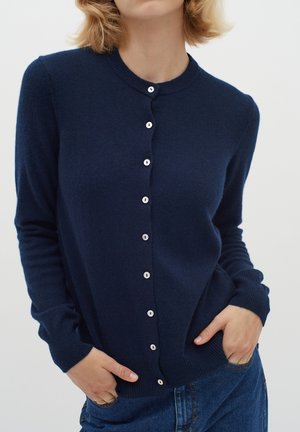 Tumed sinine kudum cardigan ümmarguse kaelusega, valgete nööpidega ees ning ribakujuliste mansettide ja alläärega. Pehme tekstuur, keha lähedane vorm.
