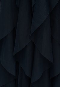 Σκούρο μπλε ύφασμα με στρώσεις και υφή, με χαλαρό υφαντό μοτίβο που δημιουργεί απαλά καταρράκτες πτυχώσεις.