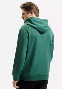 Zielona bluza z kapturem z miękkiego materiału, o luźnym kroju, z regulowanym kapturem oraz ściągaczami przy mankietach i u dołu. Brak widocznych wzorów lub ozdób.