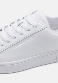 Witte leren sneaker met een gestructureerde rubberen zool, afgeronde vorm en platte veters. Beschikt over een ingebosseld logo aan de zijkant en een minimalistisch ontwerp.
