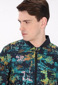 Jachetă bomber cu fermoar frontal, având o bază întunecată și modele abstracte colorate în nuanțe de teal, portocaliu, roz și galben. Guler și manșete ribbate.