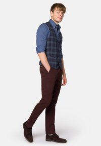 Niebieska kraciasta kamizelka na jasnoniebieskiej koszuli, w zestawieniu z brązowymi spodniami slim-fit i brązowymi zamszowymi butami. Prosty design i dopasowany krój.