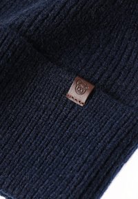 Tumesinise soonikkoega lõngast kangas, millel on pruun nahkmärk karumärgi logoga. Tekstuur on pehme, nähtavate kiudude ja tiheda õmblusega.