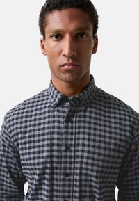 Blauw en grijs geblokt overhemd met knopen, gemaakt van een stof met een zachte textuur; heeft een klassieke kraag en donkere knopen.