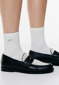 Sorte læderloafers med grå mesh-detaljer og et dekorativt bånd. Båret med lyse, ribbede sokker med et subtilt logo.