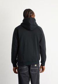 Felpa nera con un grande cappuccio regolabile e maniche raglan. Realizzata in materiale morbido e testurizzato, presenta un orlo e polsini a coste.