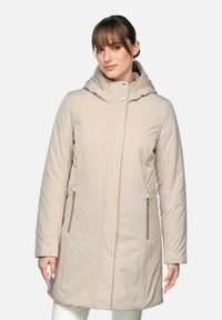 Parka beige isolée avec capuche, fermeture éclair avant et deux poches latérales avec accents en métal doré. Tissu lisse et texturé.