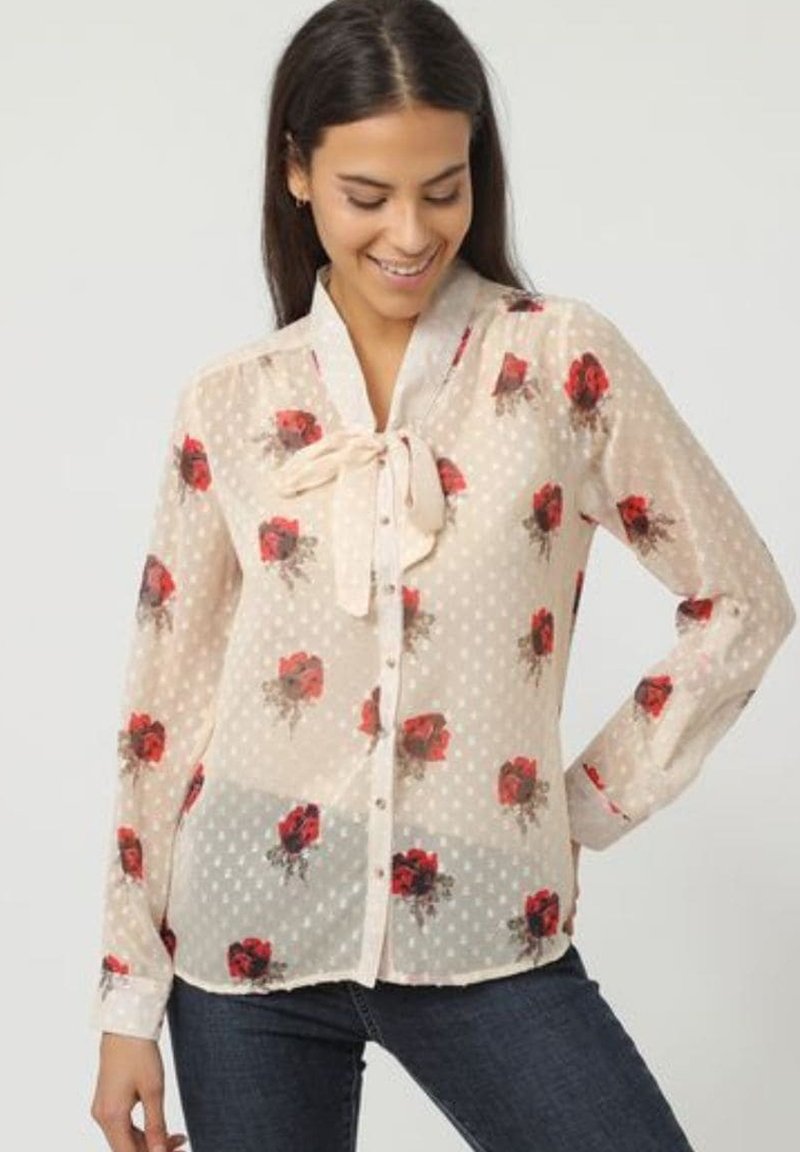 Blusa de seda color crema con un patrón de lunares y estampado floral en rojo. Detalle de cuello con lazo y cierre frontal de botones. Mangas largas con puños.