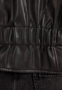 Close-up van de gerimpelde tailleband van een zwart leren jack over zwarte denim jeans, met nadruk op textuur en stikdetails.