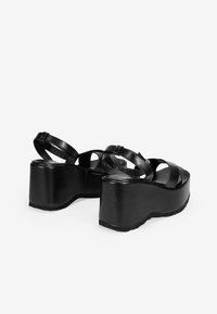 Sandalias de plataforma negras hechas de cuero suave, con múltiples correas entrecruzadas y una suela gruesa y redondeada con fondo texturizado.