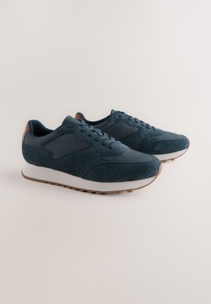 Baskets bleu marine en daim et mesh avec une semelle intermédiaire blanche, présentant une semelle extérieure en caoutchouc texturée et un accent marron au talon.