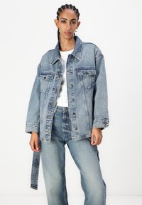 Lyseblå denimjakke med avslappet passform, med to brystlommer, knappefeste og synlig søm. Stylet med matchende jeans.