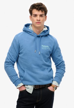 Blauwe hoodie met een kangoeroezak, capuchon met trekkoord en geborduurd logo. Draag je over een lichte gestreepte shirt, gecombineerd met donkere jeans.