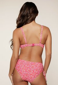Rosa mönstrad bikini-set med justerbara band och ett spänne på ryggen. Underdelen har en knytning på sidan med blommönster.