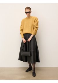 Żółty wełniany sweter, czarna skórzana spódnica midi, czarna torba, czarne buty i okulary przeciwsłoneczne. Gładka faktura, luźny fason i minimalistyczny design.