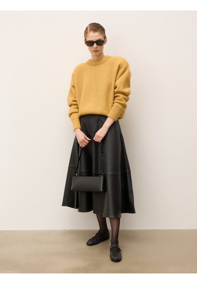 Żółty wełniany sweter, czarna skórzana spódnica midi, czarna torba, czarne buty i okulary przeciwsłoneczne. Gładka faktura, luźny fason i minimalistyczny design.