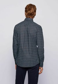 Langarmshirt van donkere stof met een geometrisch ruitpatroon in blauw. Kenmerken zijn een klassieke kraag en een getailleerde pasvorm.