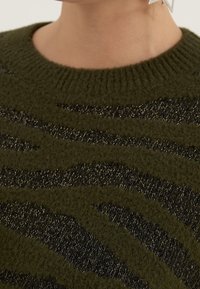 Strickpullover in olivgrün mit strukturierten, wellenförmigen schwarzen Streifen. Mit einem gerippten Kragen. Weiches Material mit leichtem Glanz.