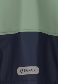 Giacca impermeabile con parte superiore verde menta e parte inferiore blu navale, con un logo sulla parte bassa. Texture liscia, design pratico.
