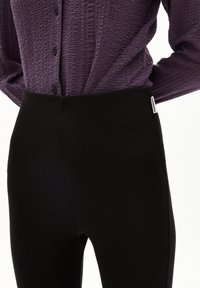 Zwarte legging met een gladde textuur en hoge tailleband, gecombineerd met een paars overhemd met een textuur en een subtiel patroon.