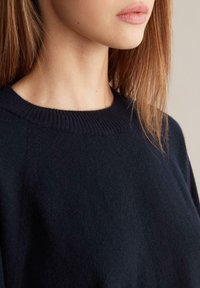 Mörkblå stickad tröja med ribbad rund halsringning. Mjuk textur, minimalistisk design och inga synliga mönster eller detaljer i metall.