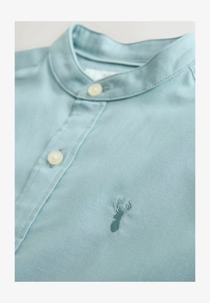 Camisa azul claro de tela suave, con cuello y cierre de botones, con un pequeño logo bordado de langosta en el pecho.